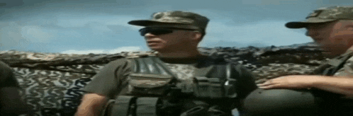 two soldiers are standing next to each other in front of a camouflaged wall .