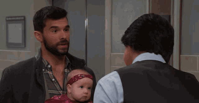 a man with a beard is holding a baby and talking to two other men