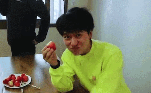 a young man is sitting at a table eating strawberries .
