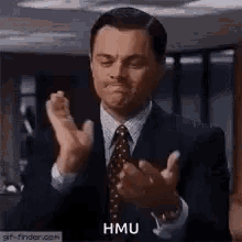a man in a suit and tie is clapping his hands and saying `` hmu '' .