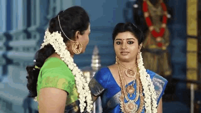 two women are standing next to each other in a temple . one of the women is wearing a blue saree .