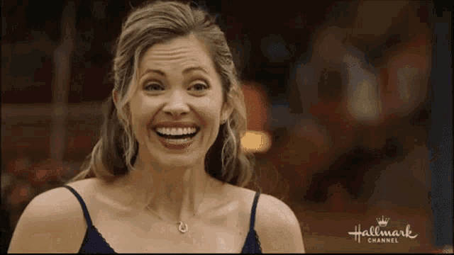 a woman in a blue tank top is smiling and wearing a necklace .
