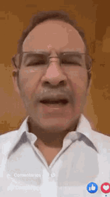 a man with glasses and a mustache is wearing a white shirt and talking .