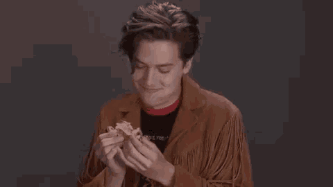 a young man in a fringed jacket is eating a hamburger with his hands .