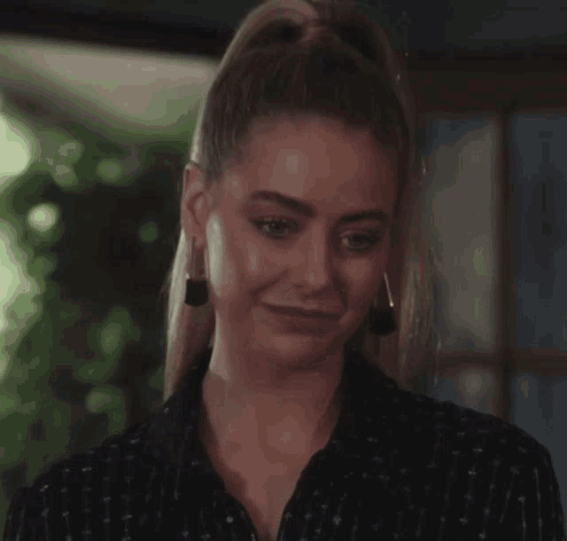 a woman with a ponytail and earrings looks at the camera