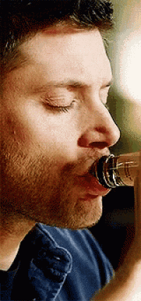 a man is drinking from a bottle with his eyes closed and his mouth open .
