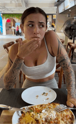 a woman covering her mouth with her hand while sitting at a table with a plate of food