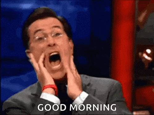 a man in a suit and tie is yawning while holding his hands to his face and saying `` good morning '' .