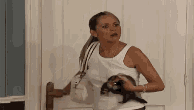 a woman in a white tank top is holding a small black animal in her arms .