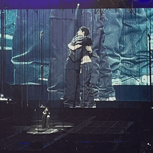 two men hugging each other on a stage with a large screen behind them