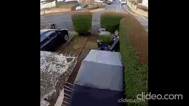 a car is parked in a driveway next to a hedge and a road .