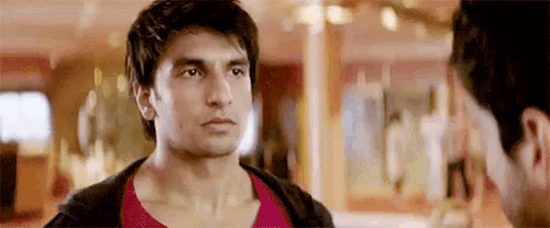 a man is looking at his reflection in a mirror while another man looks on .