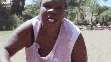 a man in a white tank top is standing in a field with his tongue out .