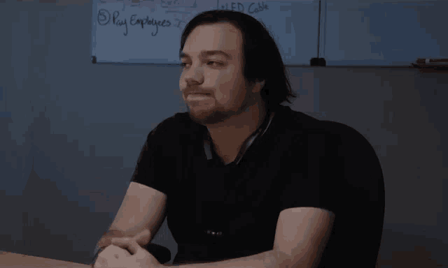 a man sits at a desk in front of a white board that says pay employees