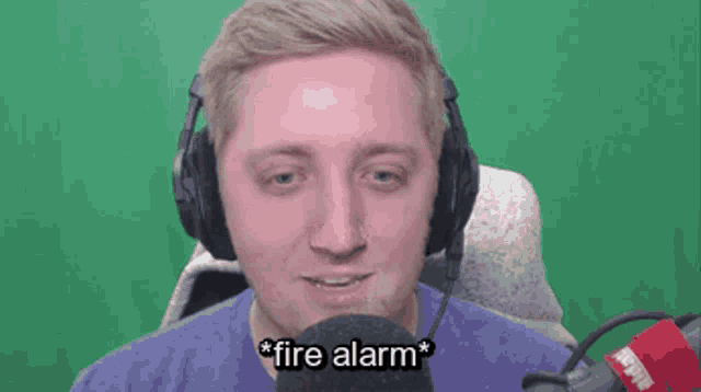 a man wearing headphones and a microphone says " fire alarm " in front of a green screen