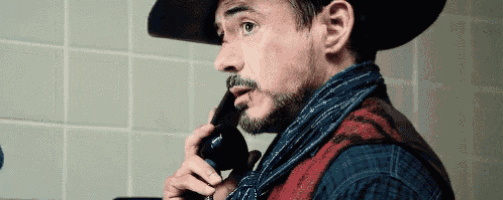 a man in a cowboy hat and scarf is talking on a cell phone .