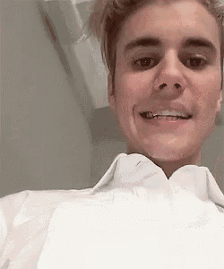 justin bieber is wearing a white shirt and smiling while taking a selfie .