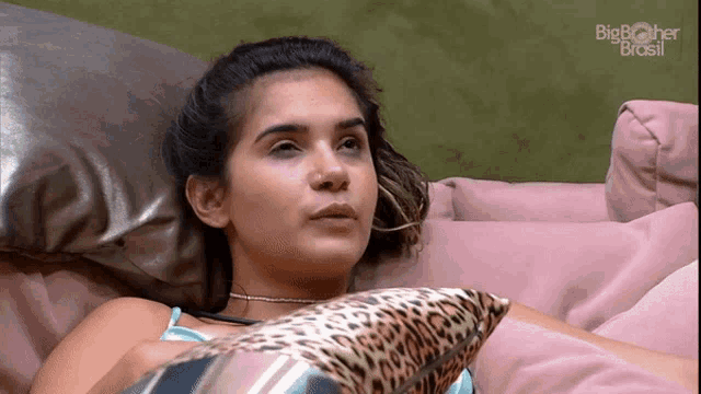 a woman is laying on a couch with a leopard print pillow and a big brother brasil logo behind her
