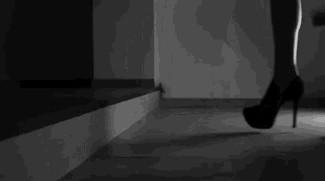 a black and white photo of a woman 's legs in high heels walking down a hallway .