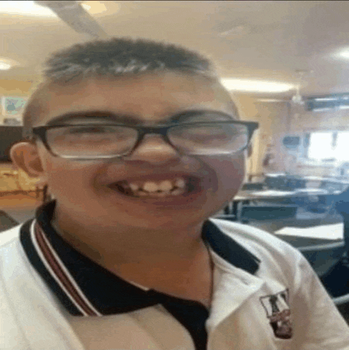 a boy wearing glasses and a polo shirt is smiling in a classroom .