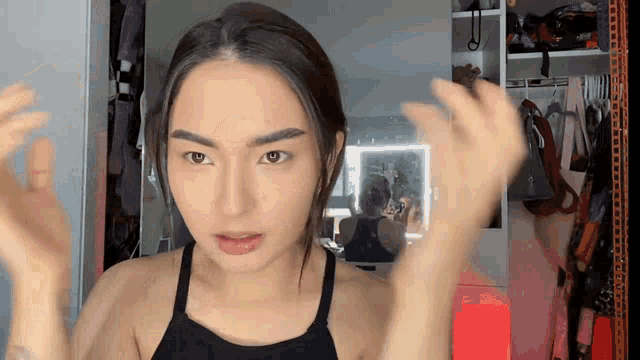 a woman in a black tank top is standing in front of a mirror with her hands outstretched