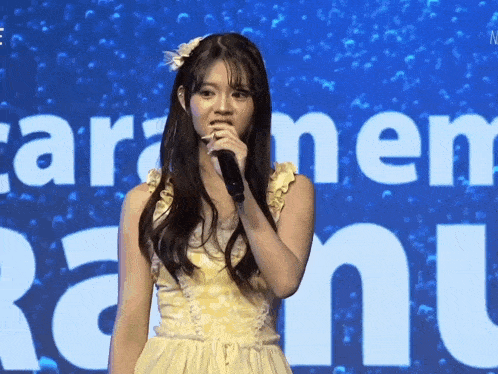 a girl singing into a microphone in front of a sign that says cara mem