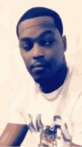 a man wearing a white t-shirt and a necklace is looking at the camera .