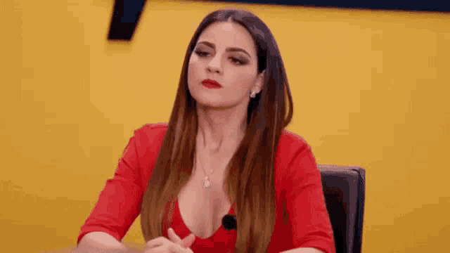 a woman in a red dress is sitting at a table and making a funny face .