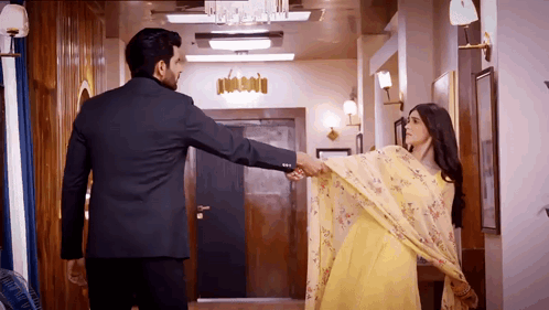 a man in a suit and a woman in a yellow dress holding hands in a hallway