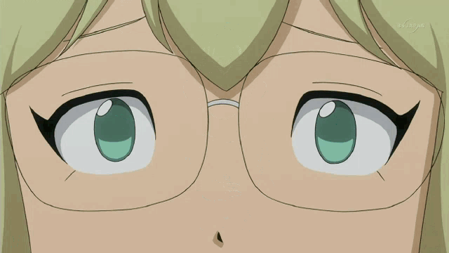 a girl with blonde hair and glasses looks at the camera in front of a tv screen that says tokyo