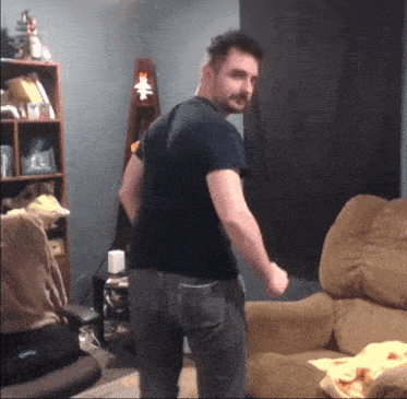 a man in a black shirt is standing in front of a brown couch
