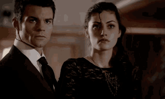 a man in a suit and tie stands next to a woman in a black top