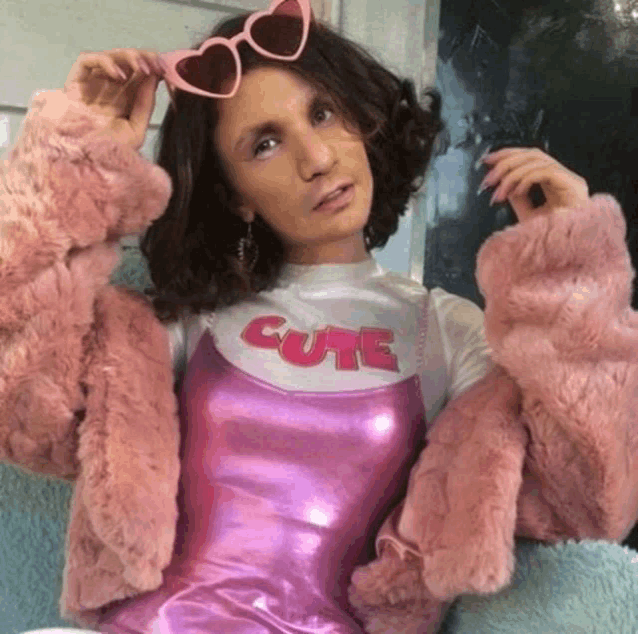 a woman wearing pink sunglasses and a pink fur coat is sitting on a couch .