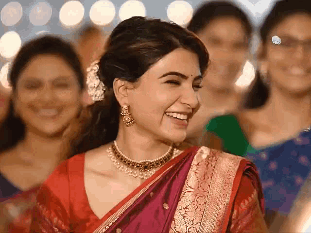 a woman in a red and gold sari is smiling in front of a group of women .