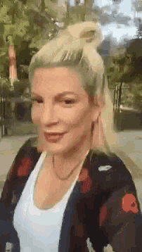 a woman with blonde hair is wearing a white shirt and a black jacket with red flowers on it .