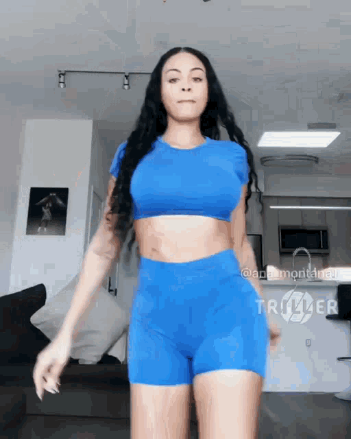 a woman wearing a blue crop top and shorts is standing in a living room