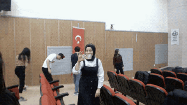 a woman in a hijab stands in front of a flag with a c on it