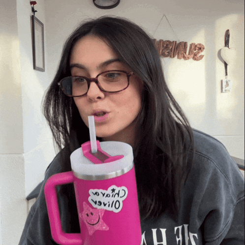 a woman wearing glasses is drinking from a pink mug with a sticker on it that says " i love you " on it