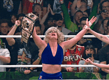 a woman in a blue top with the word bruv on it is holding a wrestling belt