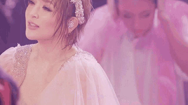 a woman in a wedding dress is singing into a microphone in front of a pink background .