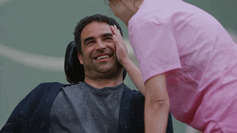 a woman in a pink shirt is touching a man 's face