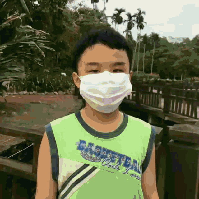a young boy wearing a mask and a green tank top that says basketball