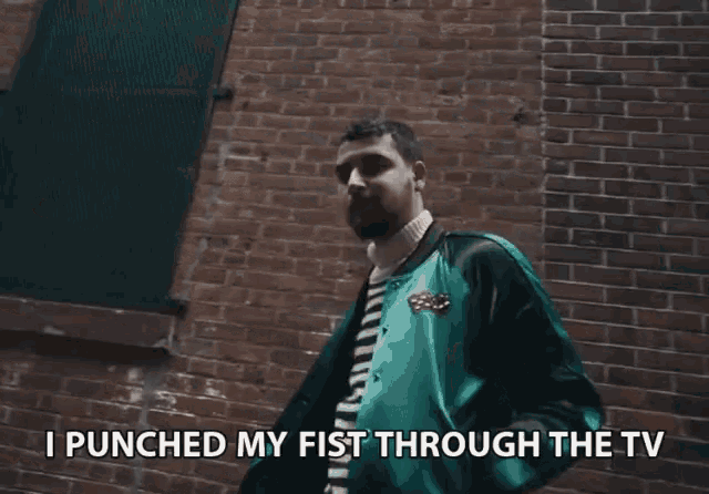 a man standing in front of a brick wall with the words i punched my fist through the tv below him