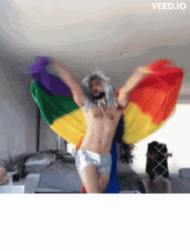 a shirtless man is dancing with a rainbow flag behind him
