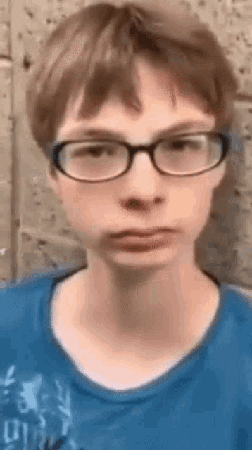 a young boy wearing glasses and a blue shirt is looking at the camera .