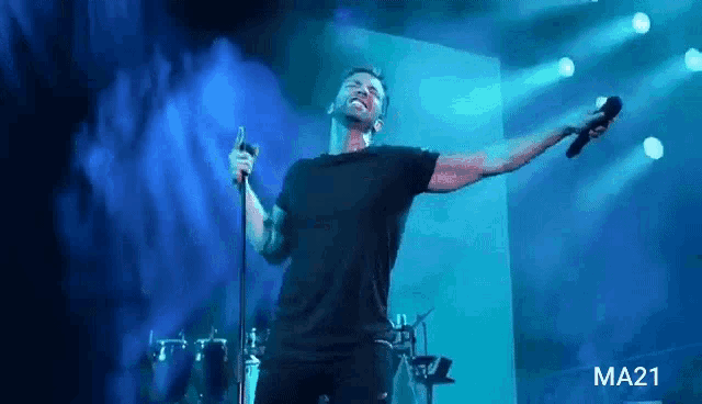 a man is singing into a microphone on a stage in front of a blue background .
