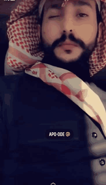a man with a beard and mustache is wearing a head scarf and a shirt that says apo-ode @