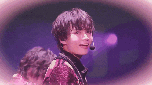 a young man wearing a microphone is standing on a stage in front of a purple background .
