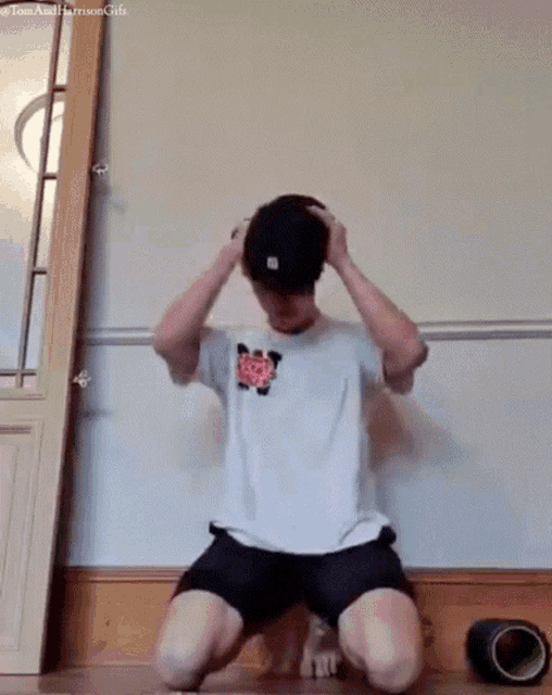 a man in a white shirt and black shorts is kneeling on the floor holding his hat .