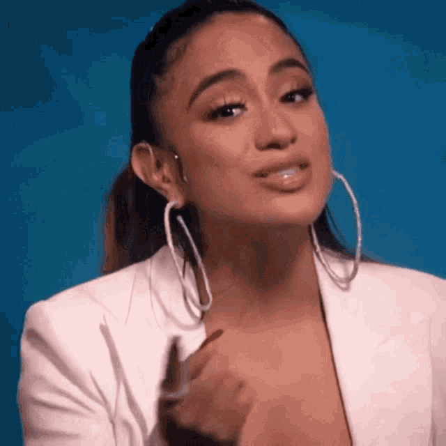a woman wearing a white jacket and hoop earrings is making a face .